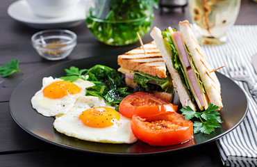 Breakfast: fried egg, spinach, tomatoes and club sandwich on plate.