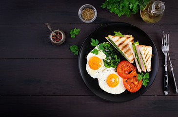 Breakfast: fried egg, spinach, tomatoes and club sandwich on plate. Top view, copy space