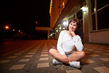 Brunette girl near glowing building on the street of night city and black background with light