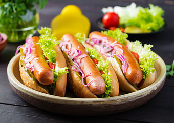 Hot dog with  sausage, pickled cucumber, tomatoes, red onions and lettuce on dark wooden background. Summer hotdog.