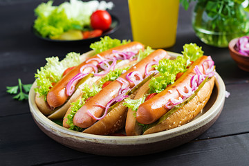 Hot dog with  sausage, pickled cucumber, tomatoes, red onions and lettuce on dark wooden background. Summer hotdog.