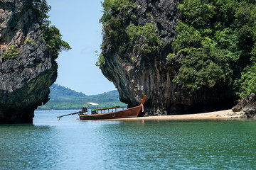 Traditional long-tail boat parks on the beach with high cliff and seascape in background