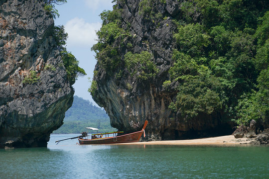 Traditional long-tail boat parks on the beach with high cliff and seascape in background