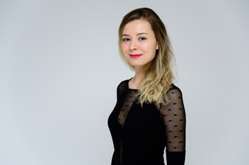 Concept of a woman talking in front of the camera. A photo of a pretty smiling girl with curly hair in a black T-shirt on a white background is standing right in front of the camera.