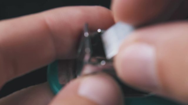 young man opens small turquoise stapler to put in metal clips on dark background extreme close view