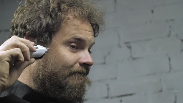 a man with a beard shaves his head with an electric trimmer. man in barbershop. 4k video. slow motion. 23.98 fps