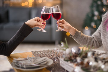 Female hands close up at christmas lights background hold wine glasses