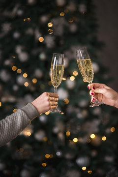 Female hands close up at christmas lights background hold champagne glasses