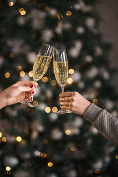 Female hands close up at christmas lights background hold champagne glasses