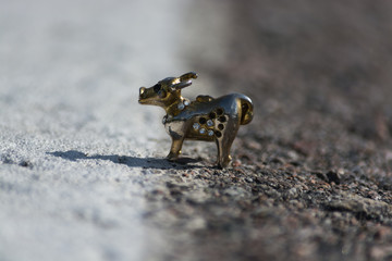 A metal miniature cow stands on asphalt. Macro shooting.