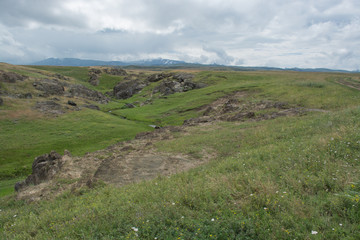 Green, grassy hill. Near the river rocks. Summer season. Nature "Kapal." Cloudy weather.