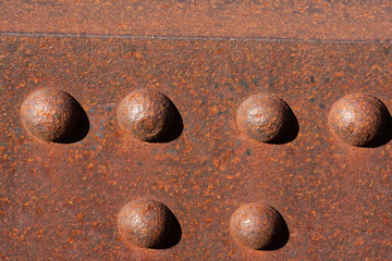 Six sunny rusty bolts head of a steel footbridge and their shadow on a rusty beam. Centered at the bottom of the image.