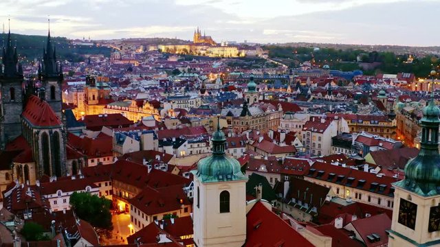 Aerial footage Church of Our Lady and old town district in Prague at twilight. Drone circling near towers and spires moving at low above illuminated streets and buildings with red tiled roof.