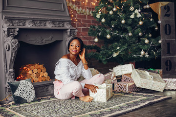 Beautiful girl in a decorated room. Woman near Christmas tree. Black lady in a white blouse