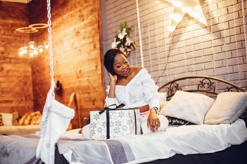 Beautiful girl in a decorated room. Woman sitting on a bed. Black lady in a white blouse