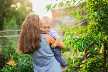 Happy beautiful mother with her son in her arms in garden