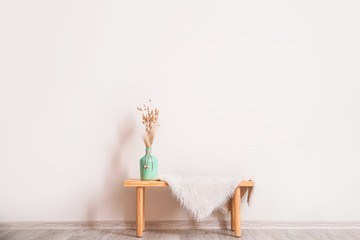 Wooden table with vase and plaid near white wall