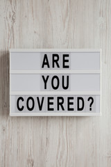 'Are you covered?' words on a modern board on a white wooden surface, top view. Overhead, from above, flat lay. Close-up.