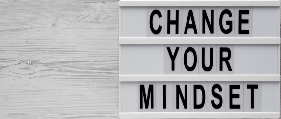 Top view, 'Change your mindset' words on a modern board on a white wooden background. Overhead, from above, flat lay. Copy space.