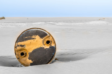 an old and used oil drum buried in sand in an open desert 