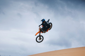 Fototapeta na wymiar Motorcyclist on a cross-country motorcycle jump from the sand dune
