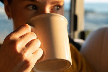 The girl holds a mug in her hands and drinks a drink from it. Close up.