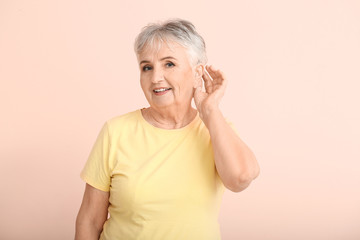 Senior woman with hearing aid on color background