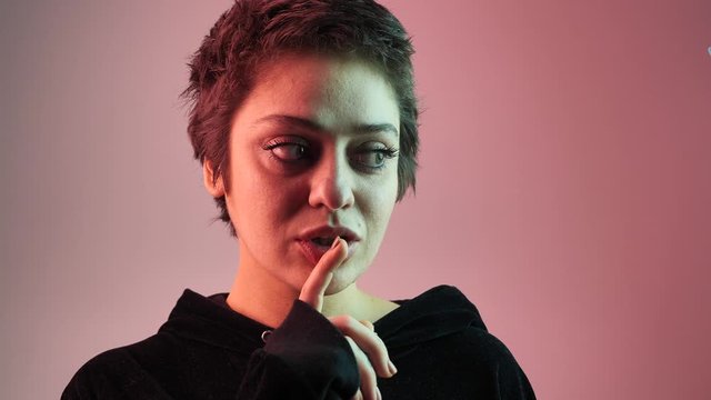 close-up female teenager puts his finger to his lips, a gesture of silence or secret against the background of neon. 4k