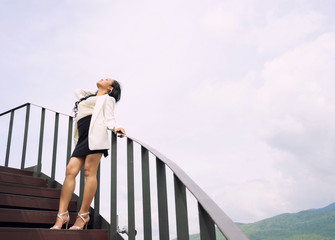 Young Asain beautiful woman standing on stairs feeling freedom face up over sky background, Thailand.