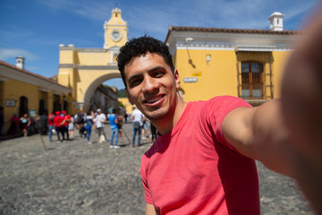 Young Hispanic man taking a self in the city of Antigua Guatemala with the Santa Catalina arch behind