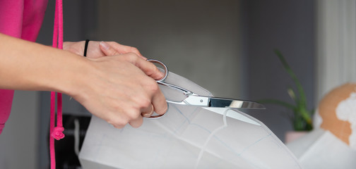 Hand with steel scissors cutting sewing pattern, tailor designing concept.