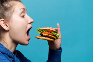 The girl opened her mouth wide and is going to eat a burger