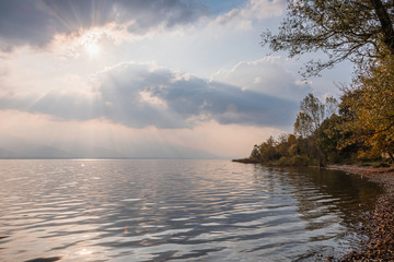 Light beams leaking through the clouds at sunset and reflection in the lake.