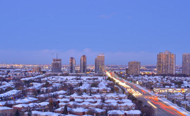 Ariel view of snow covered rooftops of north american neighborhood houses in Mississauga, Ontario, Canada. Light trails of head and tail lights cars going on the highway in the evening