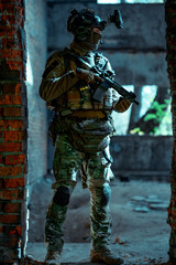 Man in uniform with machine gun and night-vision device inside broken building. Airsoft soldier in night building, beside two walls. Vertical photo