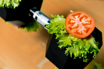 A slice of fresh tomato and salad lie on a large dumbbell.