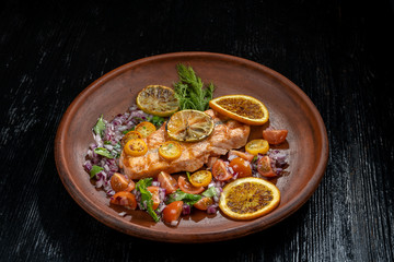 Grilled salmon and vegetables. Laid on a beautiful clay plate, sprinkled with onions, dill and tomatoes.