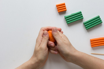 Woman hands holding orange piece of polymer clay to make it soften and warm to work with it on...