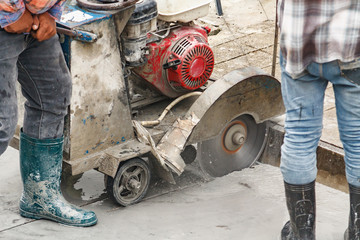 Worker using diamond saw blade machine cutting concrete road at construction site