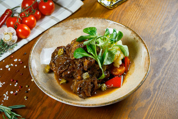 Delicious Italian veal steak Ossobuco alla Milanese stew with gremolata and vegetable on wooden background. Close up, selective focus. Tasty restaurant food.