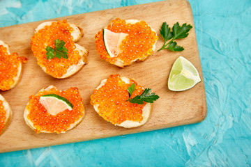 Salmon red caviar in bowl and Sandwiches with on wooden cutting board on blue background copy space. Top view.