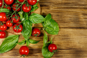 Fresh cherry tomatoes with green basil leaves on a wooden table. Top view