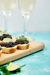 Sandwiches with black caviar. Sturgeon black caviar in wooden bowl, sandwiches and champagne on blue background copy space.