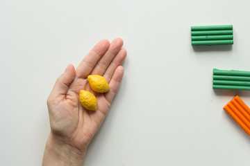 Two handmade small lemons made from polymer clay on woman hand on white background