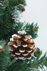 Merry christmas and a happy new year! Green Christmas tree lightly dusted with snow. Plastic Christmas tree on a light background with artificial berries and natural pine cones.
