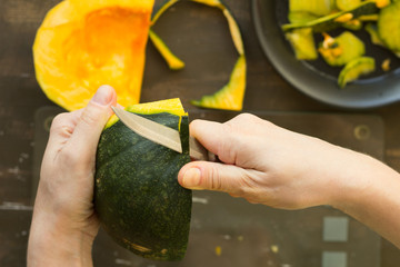 Peeling off pumpkin with ordinary knife by woman hand on wooden background