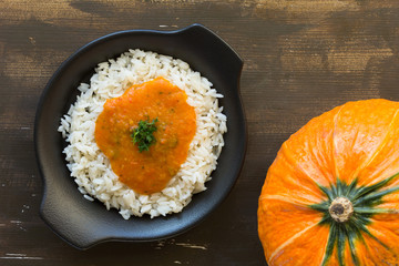 Rice with pumpkin sauce on black plate on wooden background