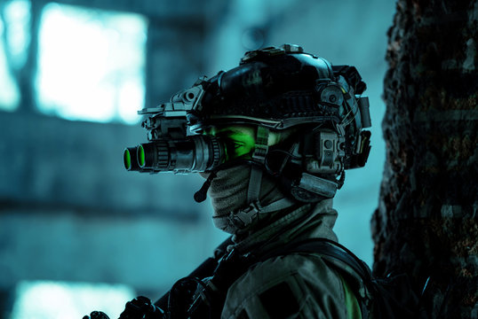 Closeup man uniform with machine gun and turned on night vision device. Airsoft soldier with green light on face in night building. Side view