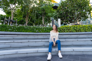 Wide angle portrait of sexy Asian woman sitting on step in the city garden