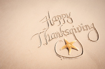 Calligraphy Happy Thanksgiving message handwritten on the beach with decorative starfish with smooth sand copy space